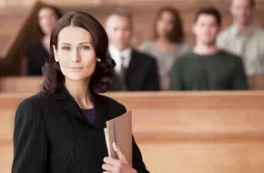 A woman is standing in front of a group of people in a courtroom holding a book.