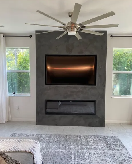 A living room with a flat screen tv mounted on the wall and a ceiling fan.