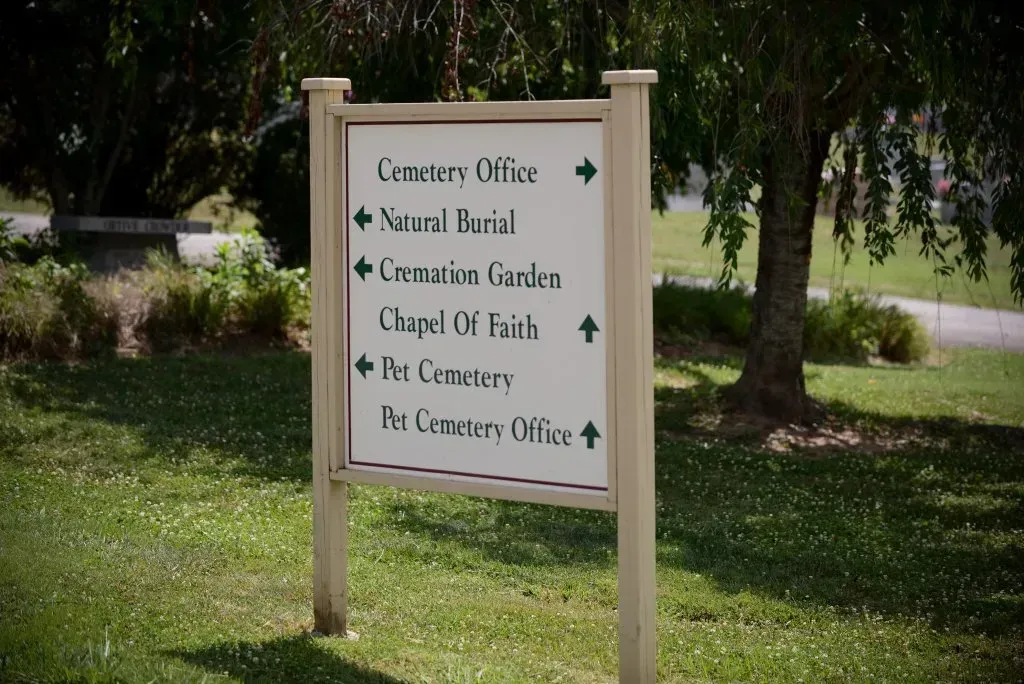 Signpost at a cemetery with directions to the office, burial sites, chapel, and gardens.