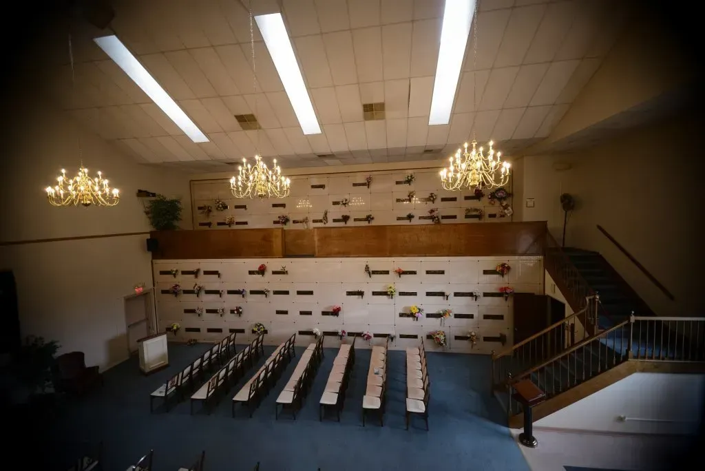 Interior of a mausoleum, rows of crypts on wall, tables and chairs below. Staircase on right.