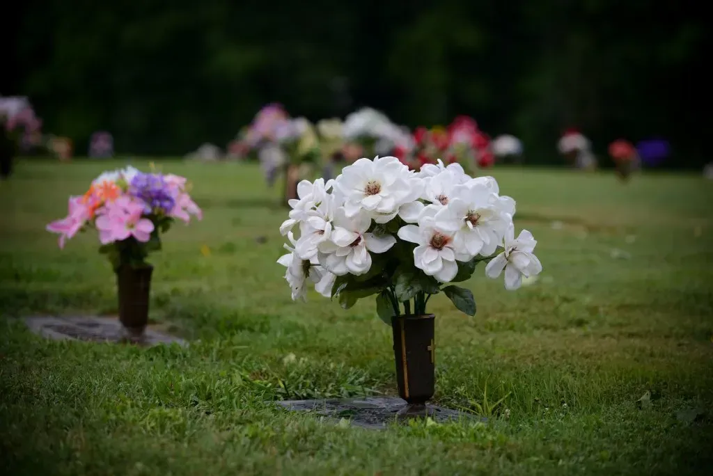 White and pink flowers in vases on green grass at a cemetery.