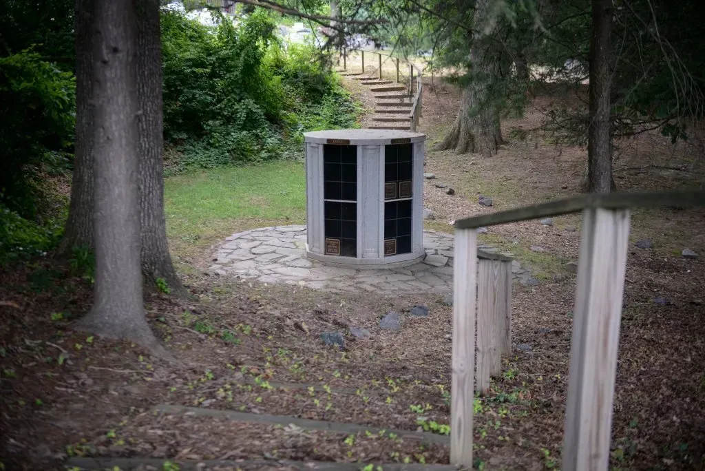 A gray structure with doors sits on a stone base, steps lead up a hill.
