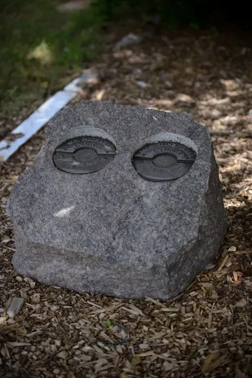 Stone sculpture with two circular carved details on a bed of wood chips.