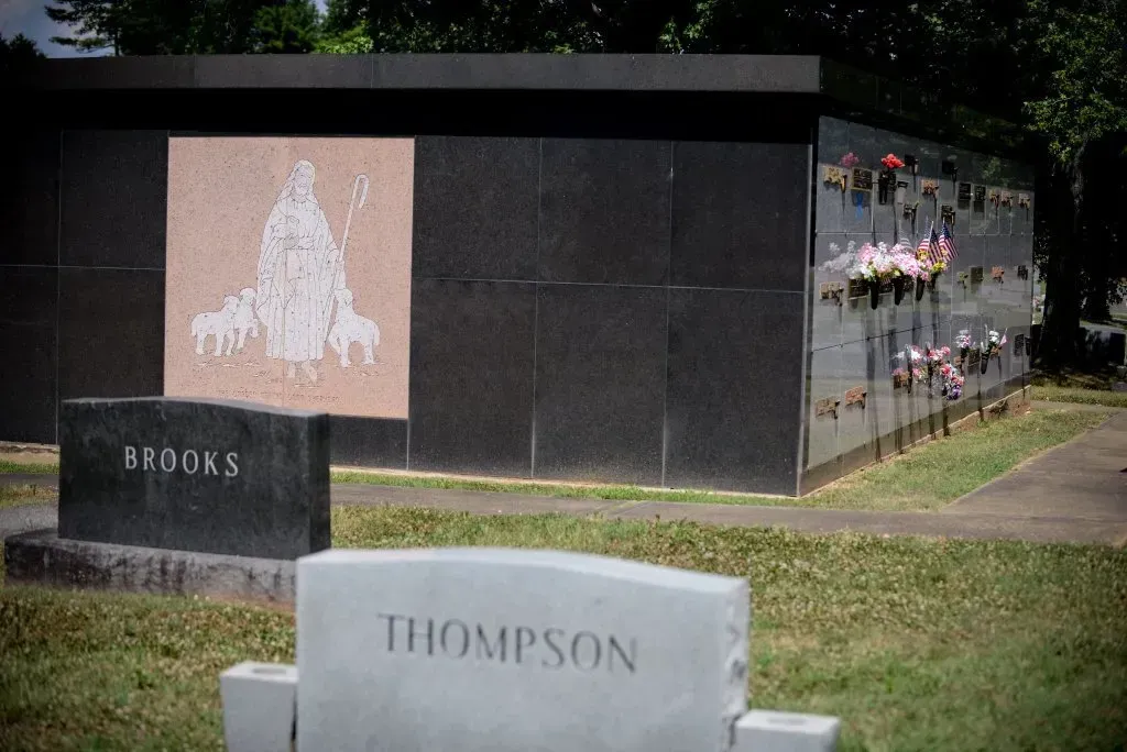 Mausoleum and tombstones in a cemetery, featuring a pink mosaic and black granite structures.