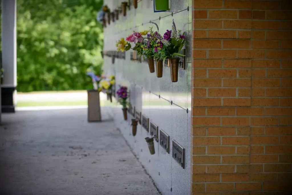Wall of memorial niches with flowers in vases, next to a brick wall.