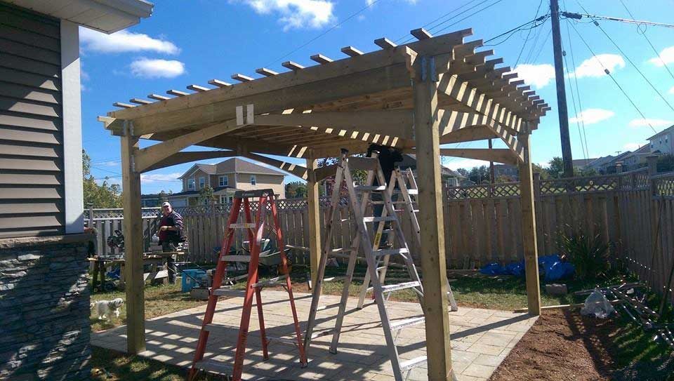 A wooden pergola is being built in the backyard of a house.