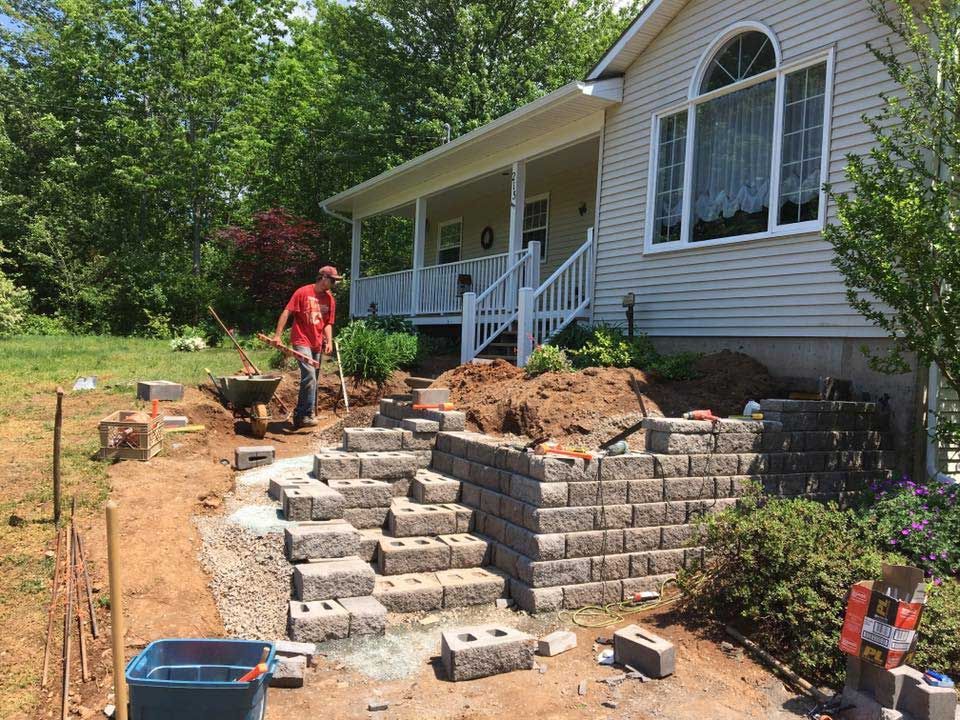 A man is working on a brick wall in front of a house.