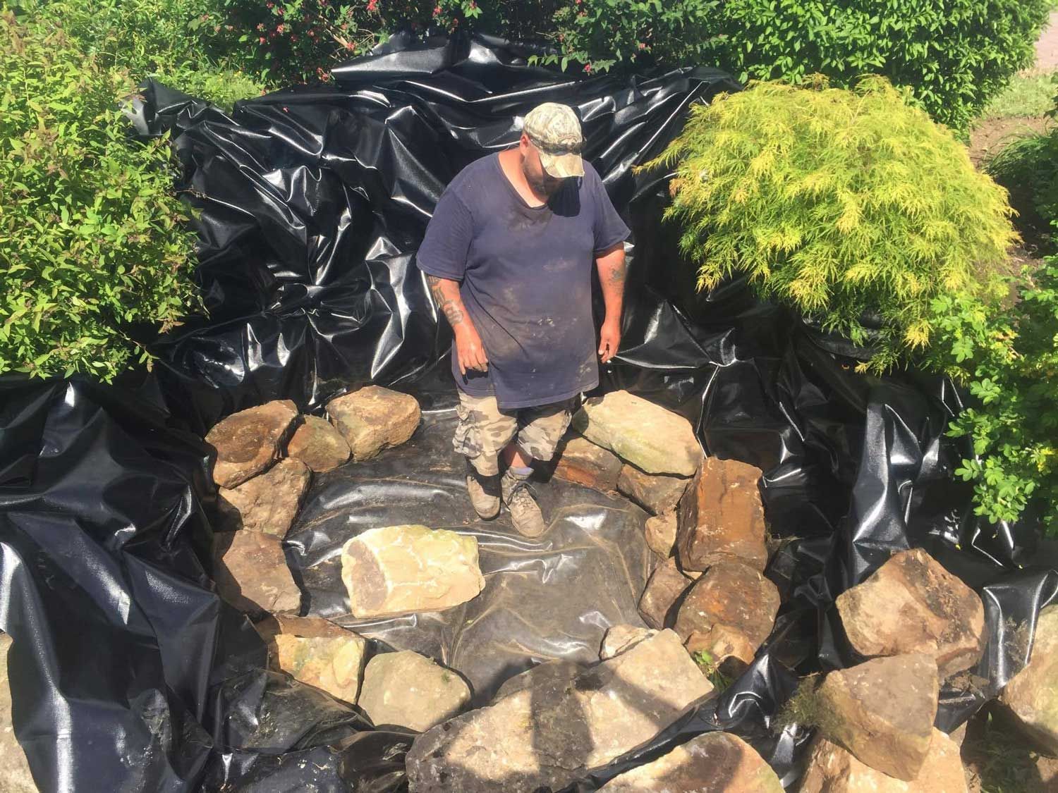 A man is standing in a pond surrounded by rocks and trees.