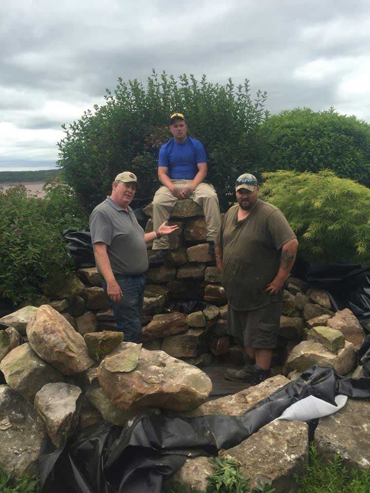 Three men are standing around a pile of rocks.