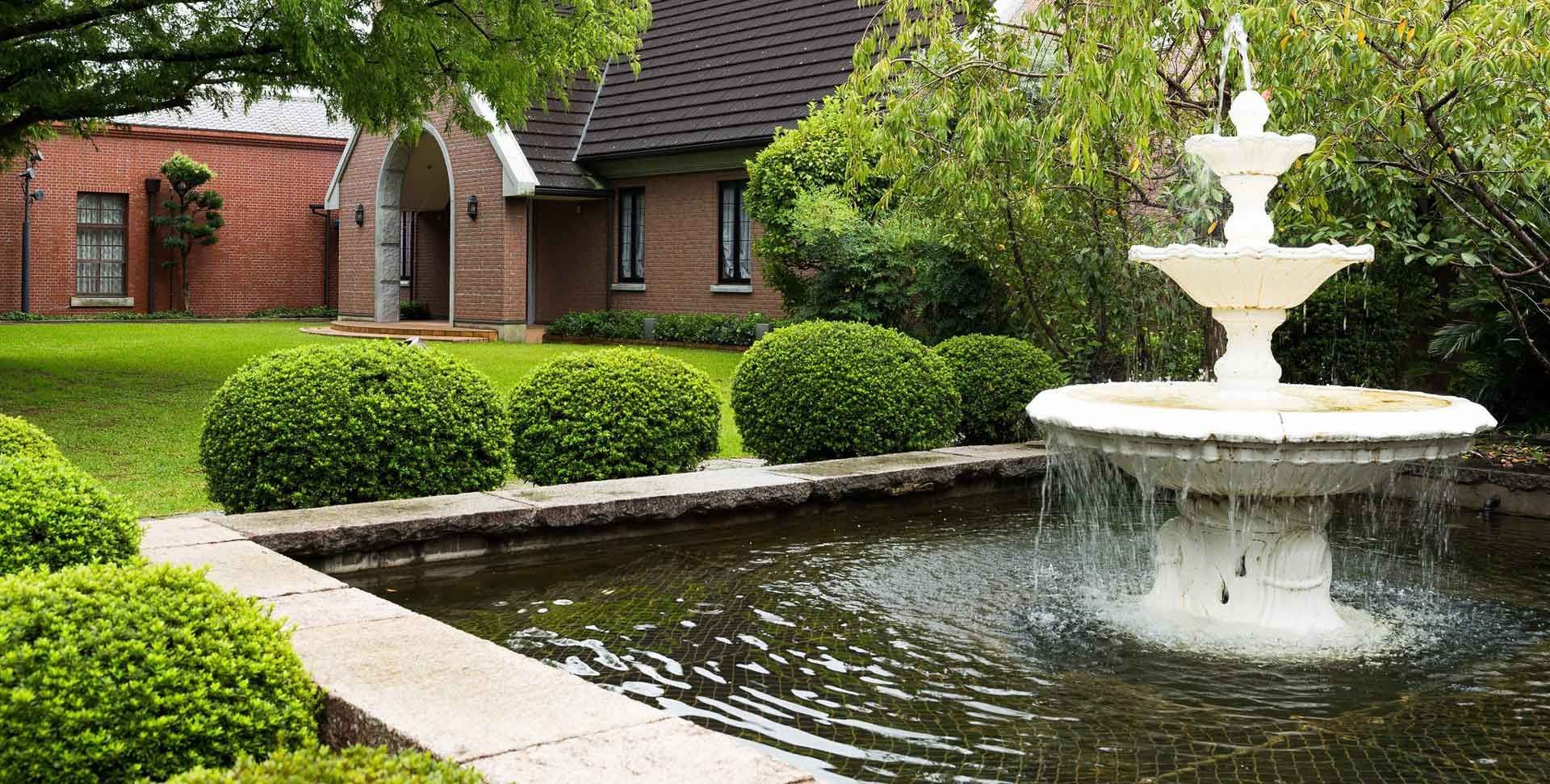 There is a fountain in the middle of a pond in front of a house.