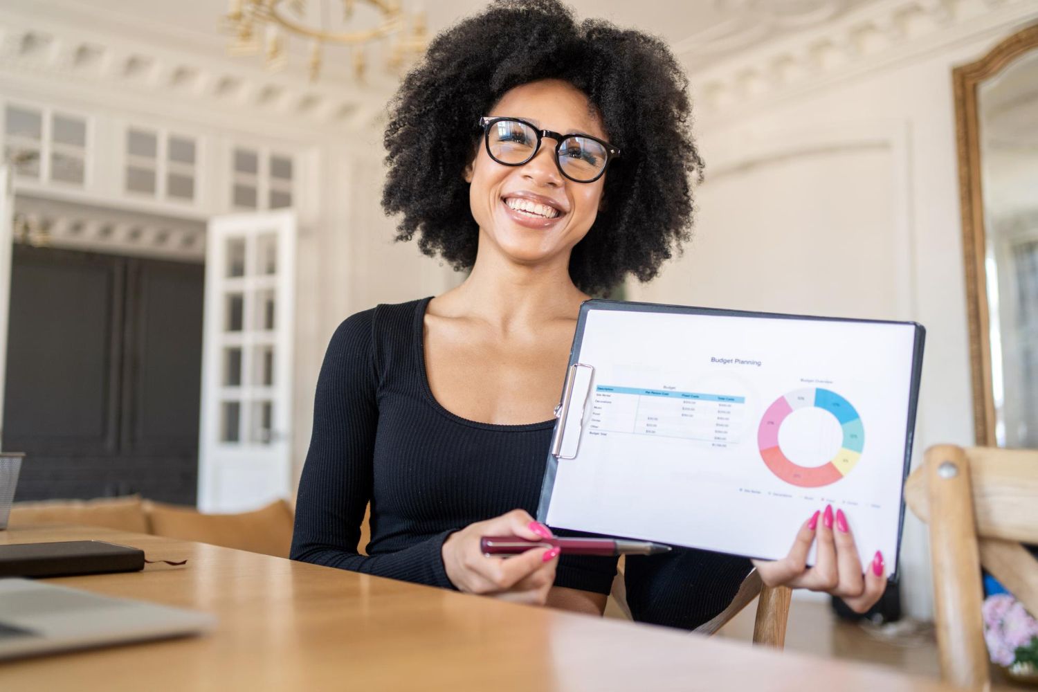 Woman in glasses holding presentation, showing pie chart and smiling.