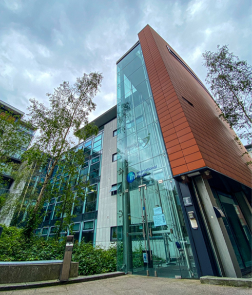 Modern building with glass facade, brown siding, and trees. Cloudy sky.