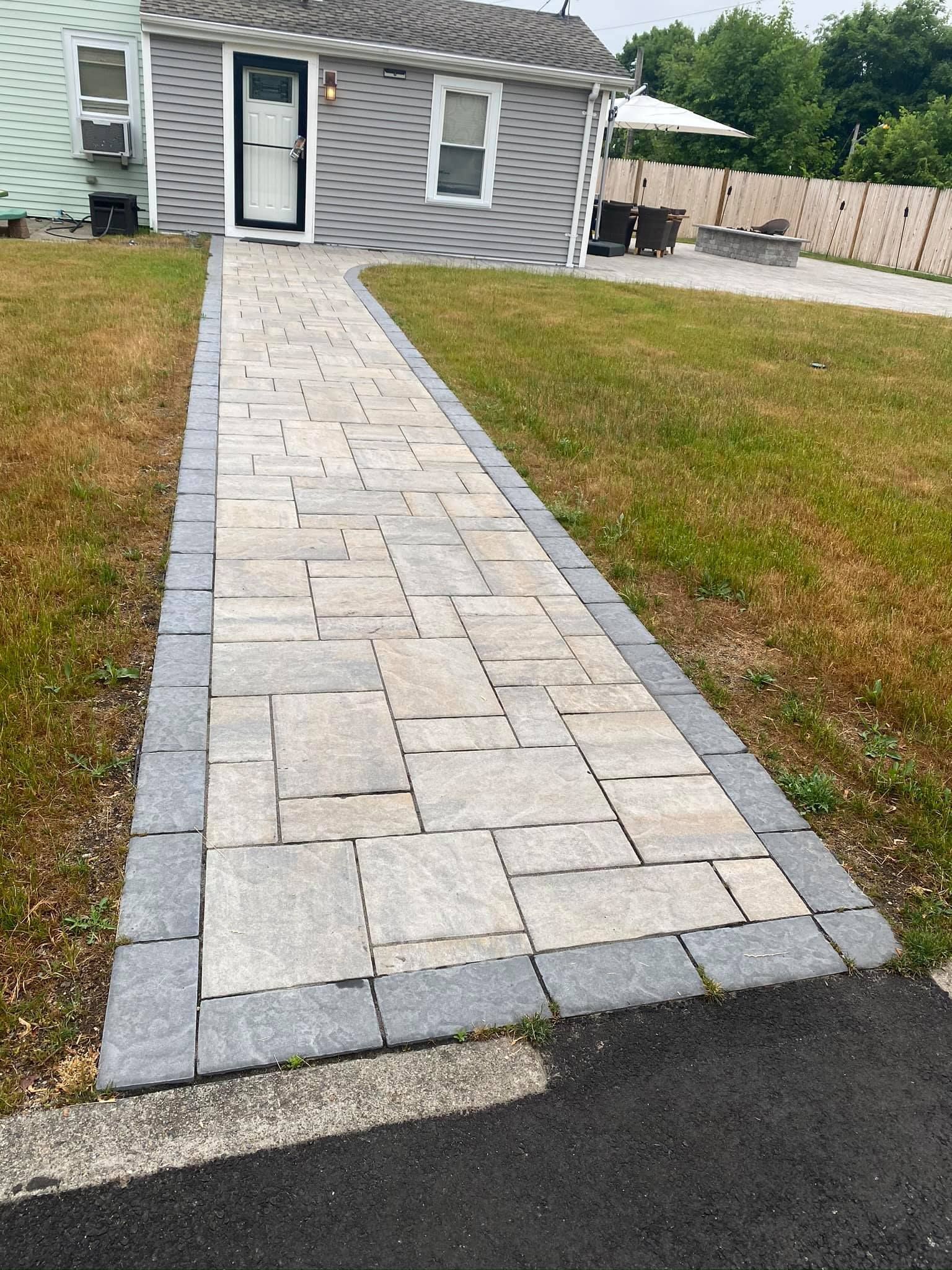 A brick walkway leading to a house with a lawn in front of it.