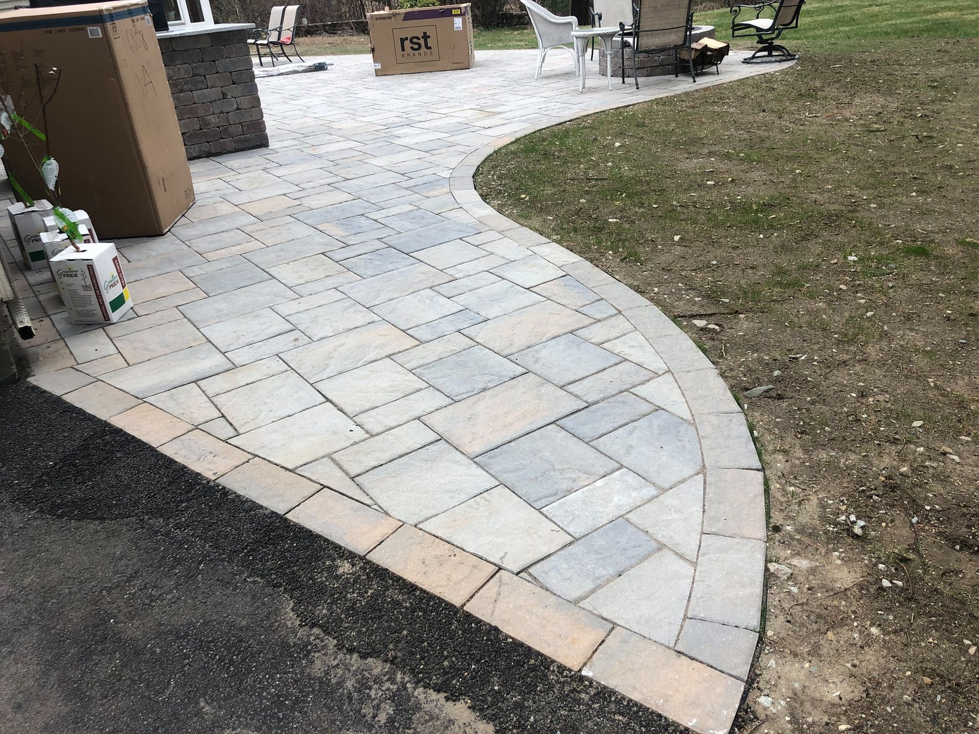 A brick walkway leading to a patio in a backyard.