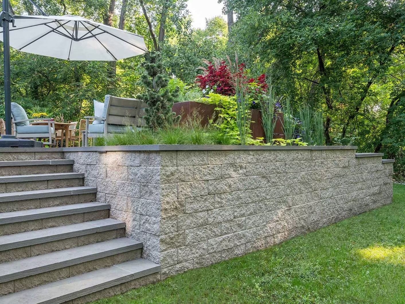 A stone wall with stairs leading up to it and an umbrella in the backyard.