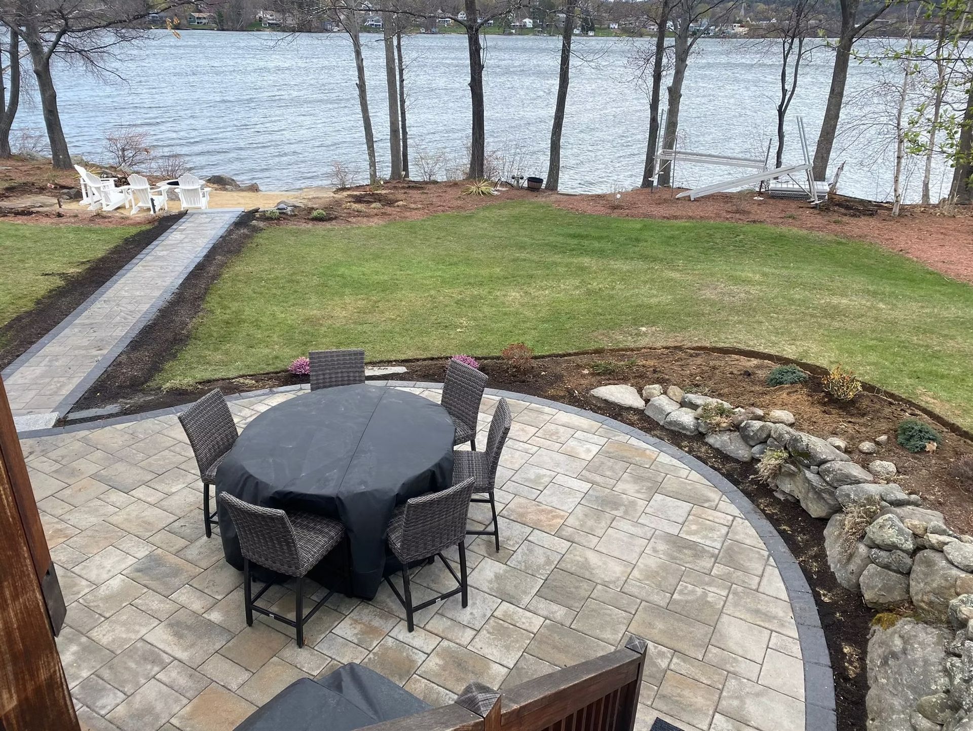 A custom patio made by Able's Landscaping with a table and chairs and a lake in the background.