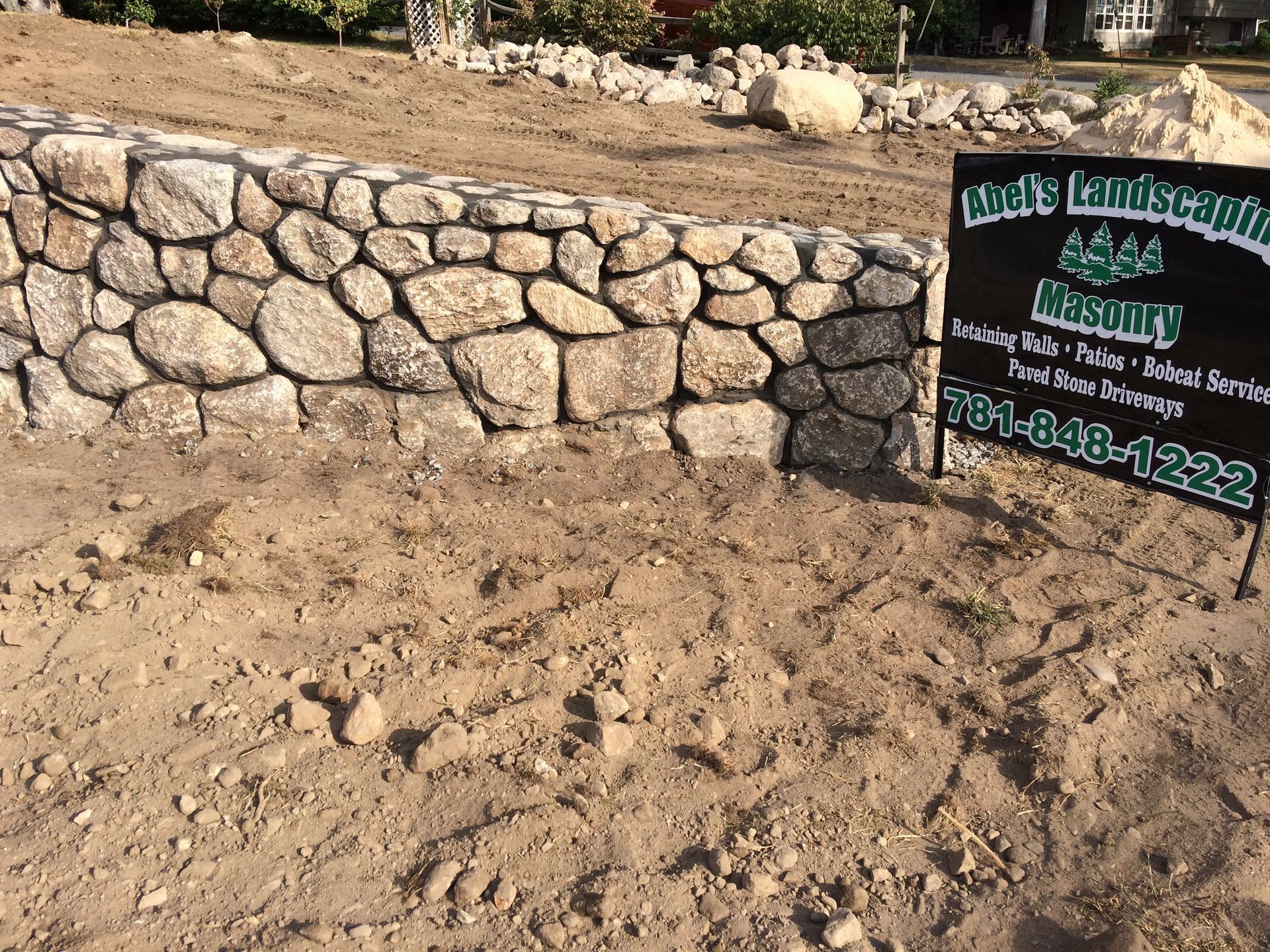 Stone retaining wall construction site with a business sign.