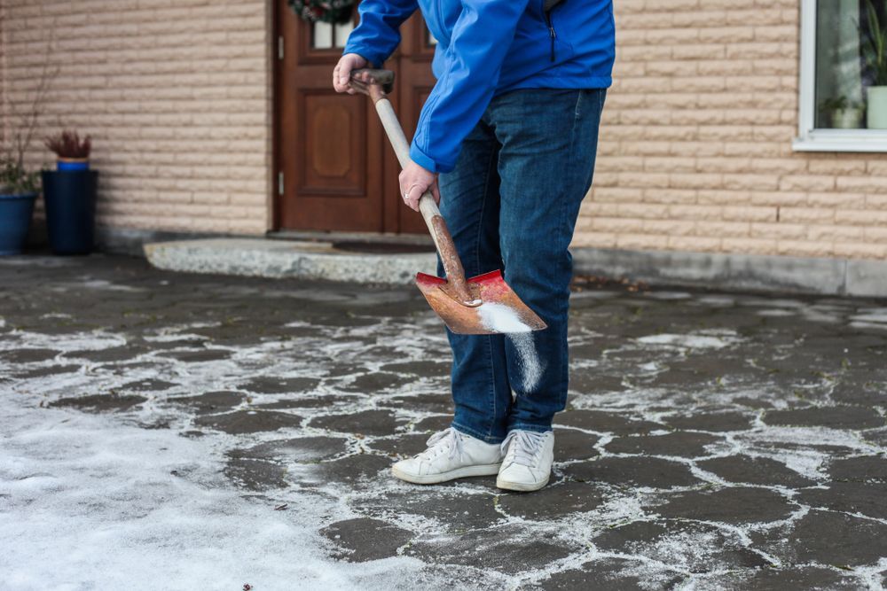 A man is shoveling snow from the sidewalk in front of a house.