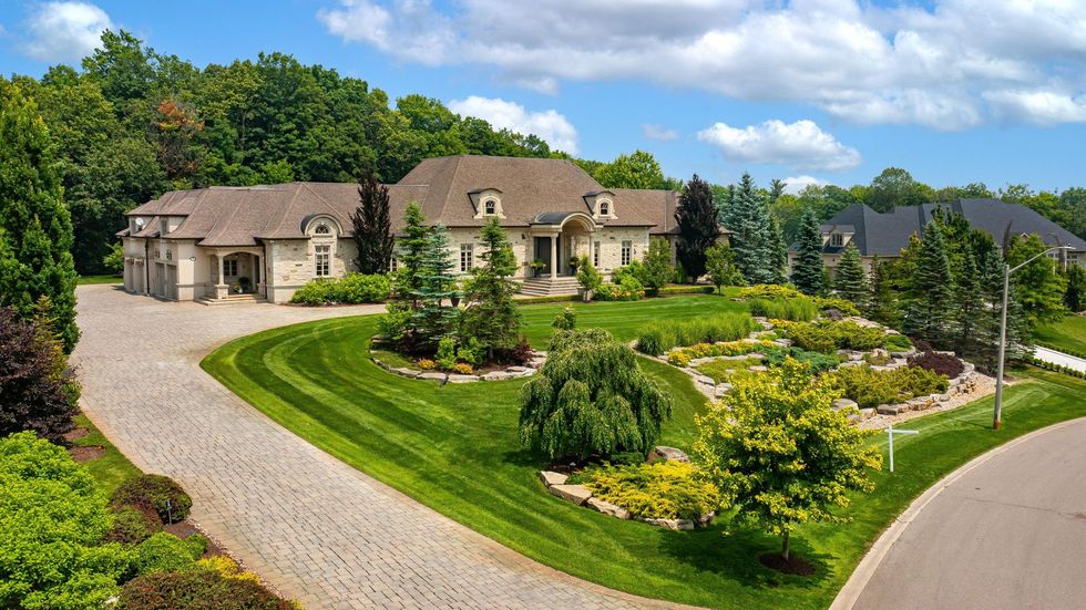 A large house with a driveway leading to it is surrounded by trees and bushes.