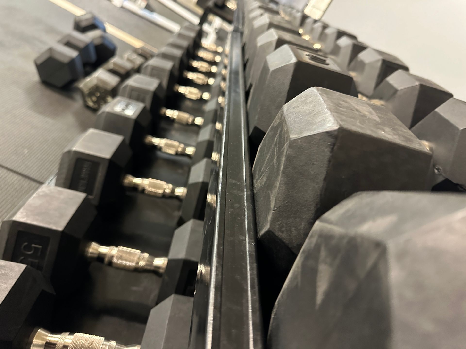 A row of black dumbbells are lined up in a gym