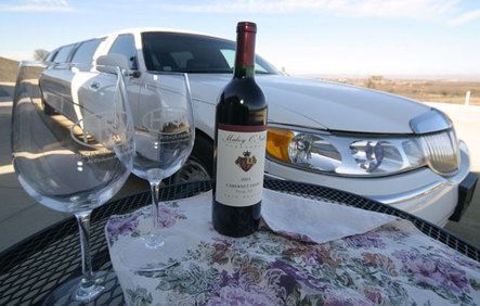 A bottle of wine and two glasses are on a table in front of a limousine.