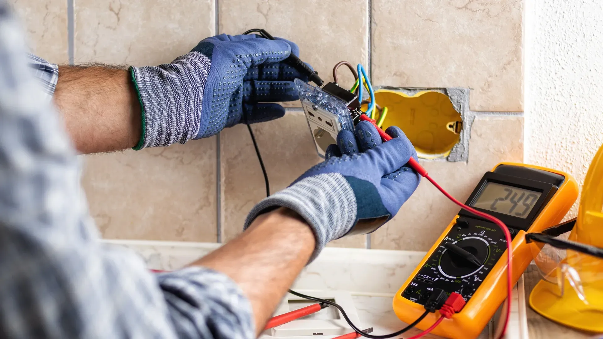 An electrician is working on an electrical outlet with a multimeter.