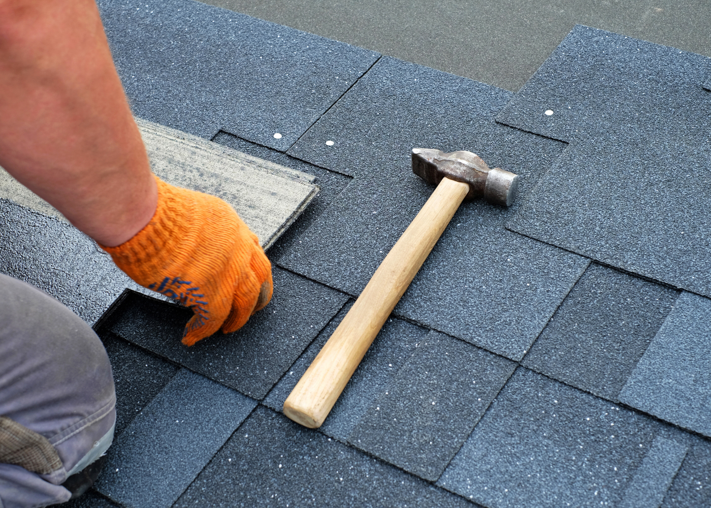 Roofing worker setting shingles with a hammer on a gray shingled roof
