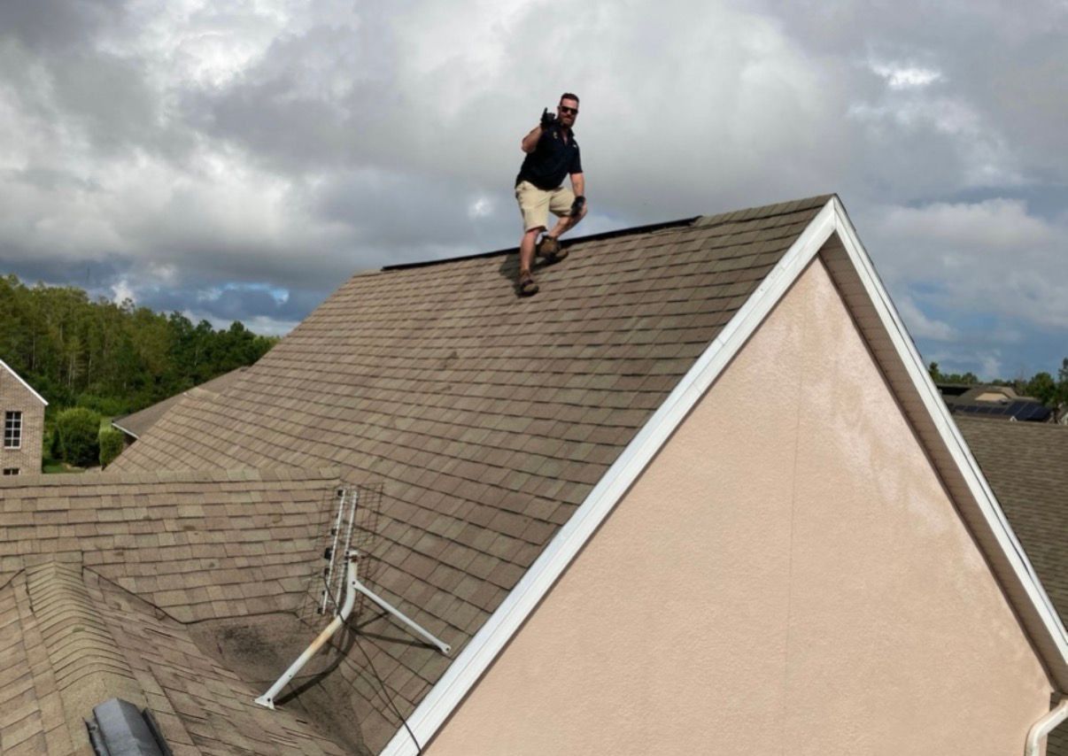 Person kneeling on a shingled roof under cloudy skies