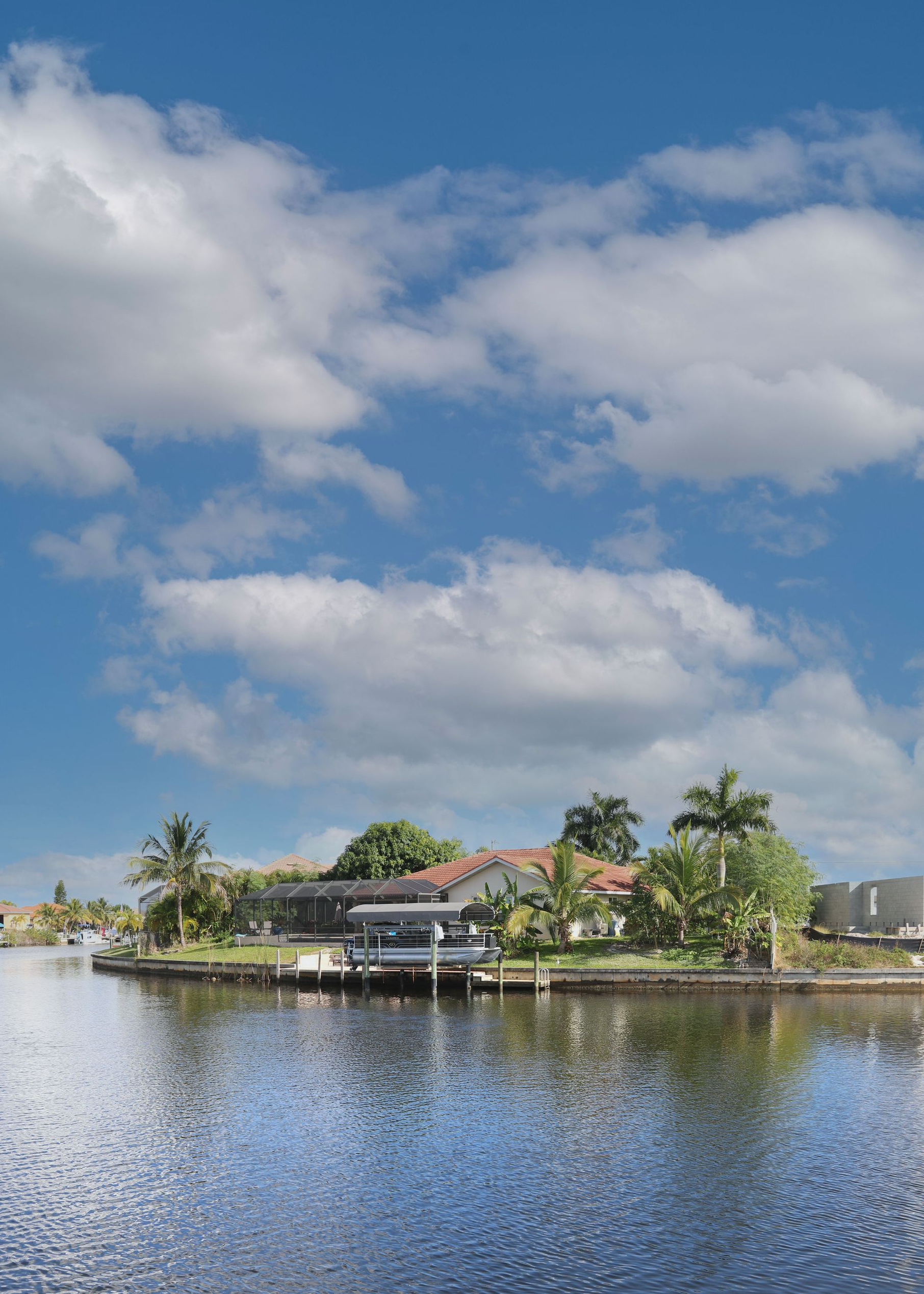 Tropical waterfront homes beside calm water under a blue sky with large clouds