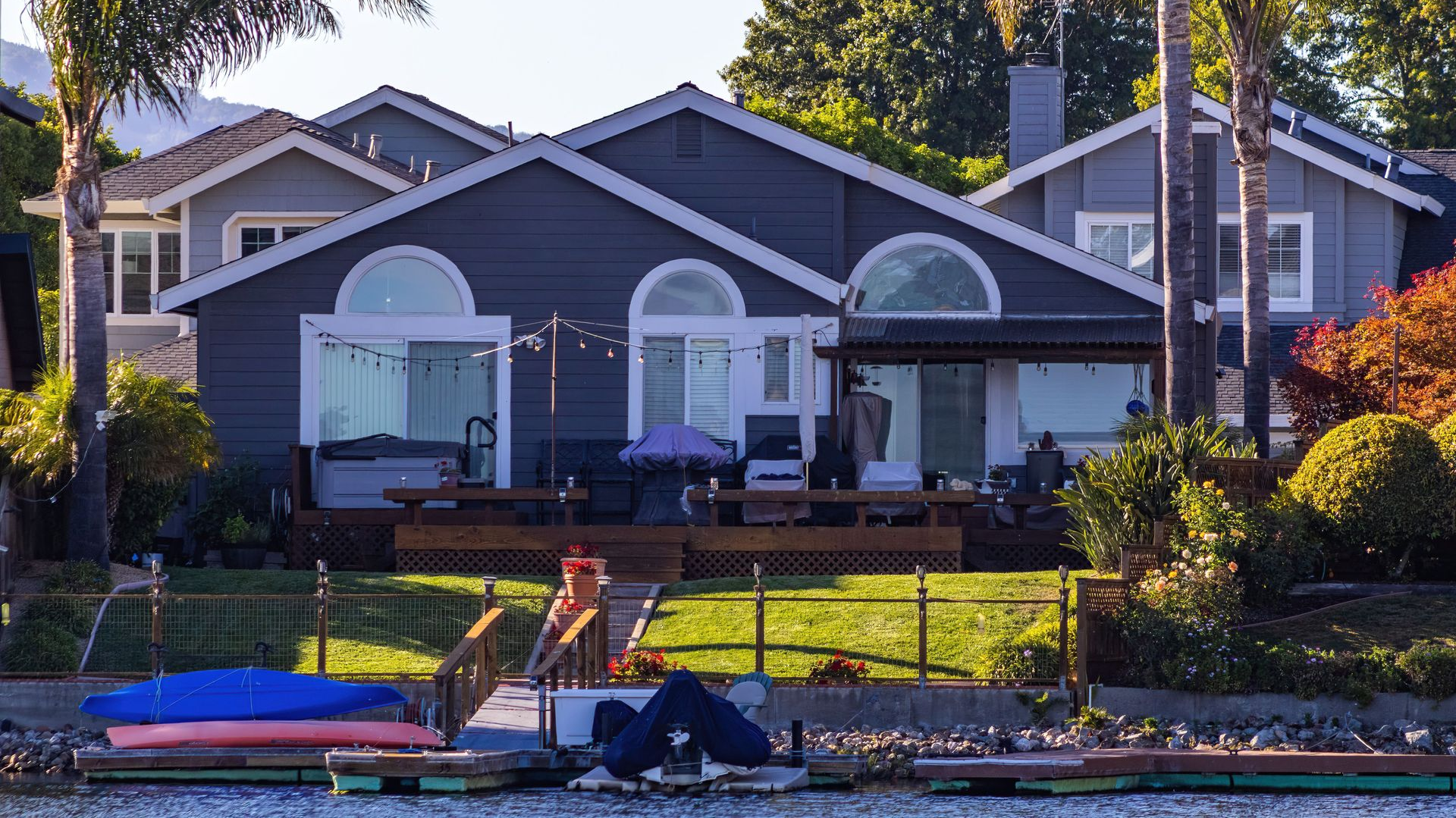 Waterfront house with white arches, dock, and a kayak by the shore at sunset.