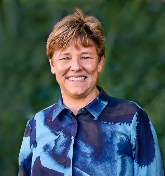 A woman is sitting at a desk with a laptop and a vase of flowers.