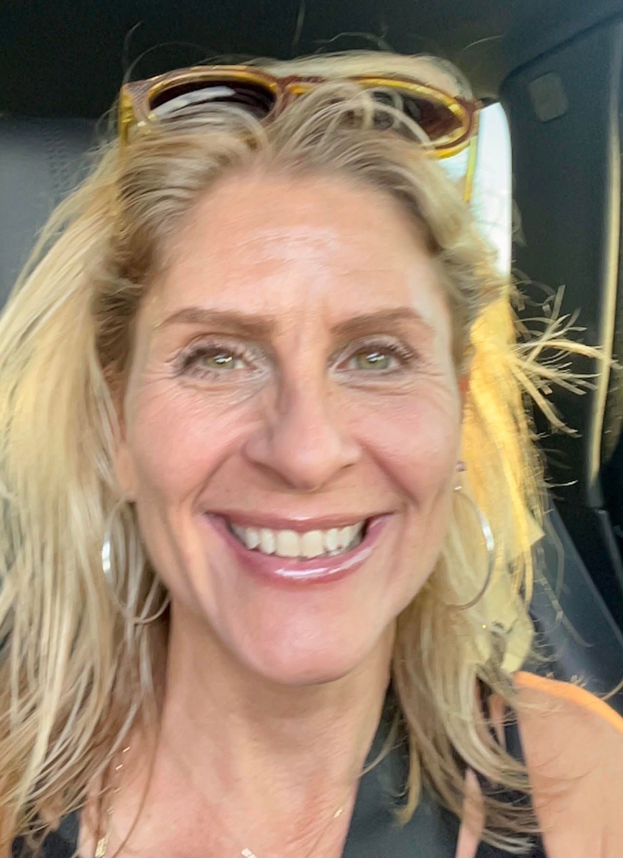 A woman wearing sunglasses is smiling while sitting in a car.
