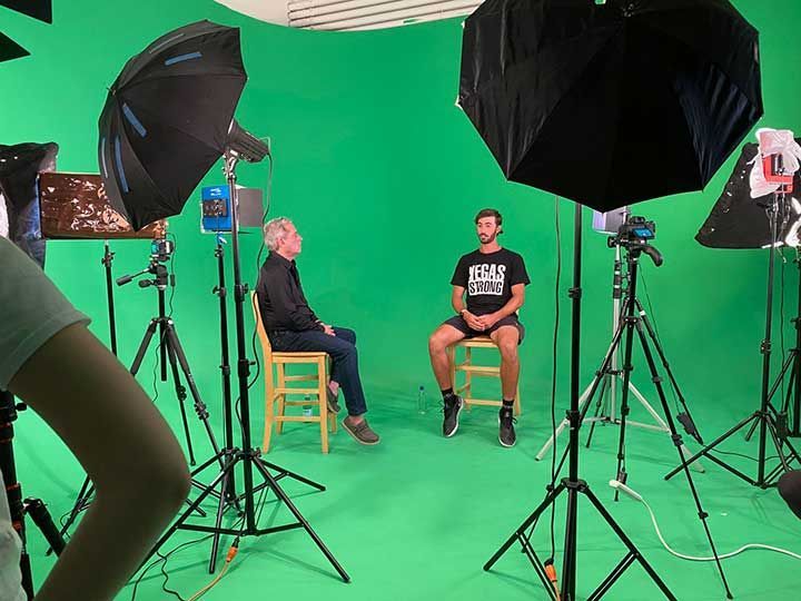 A man is sitting in a chair in front of a green screen in a studio.