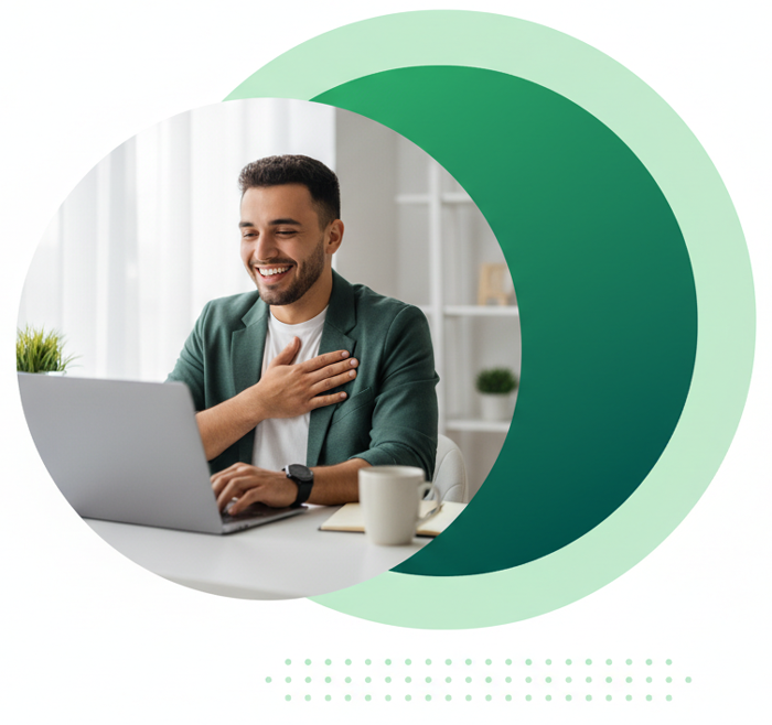 A smiling person in a green jacket sits at a desk, typing on a laptop with one hand on their chest.