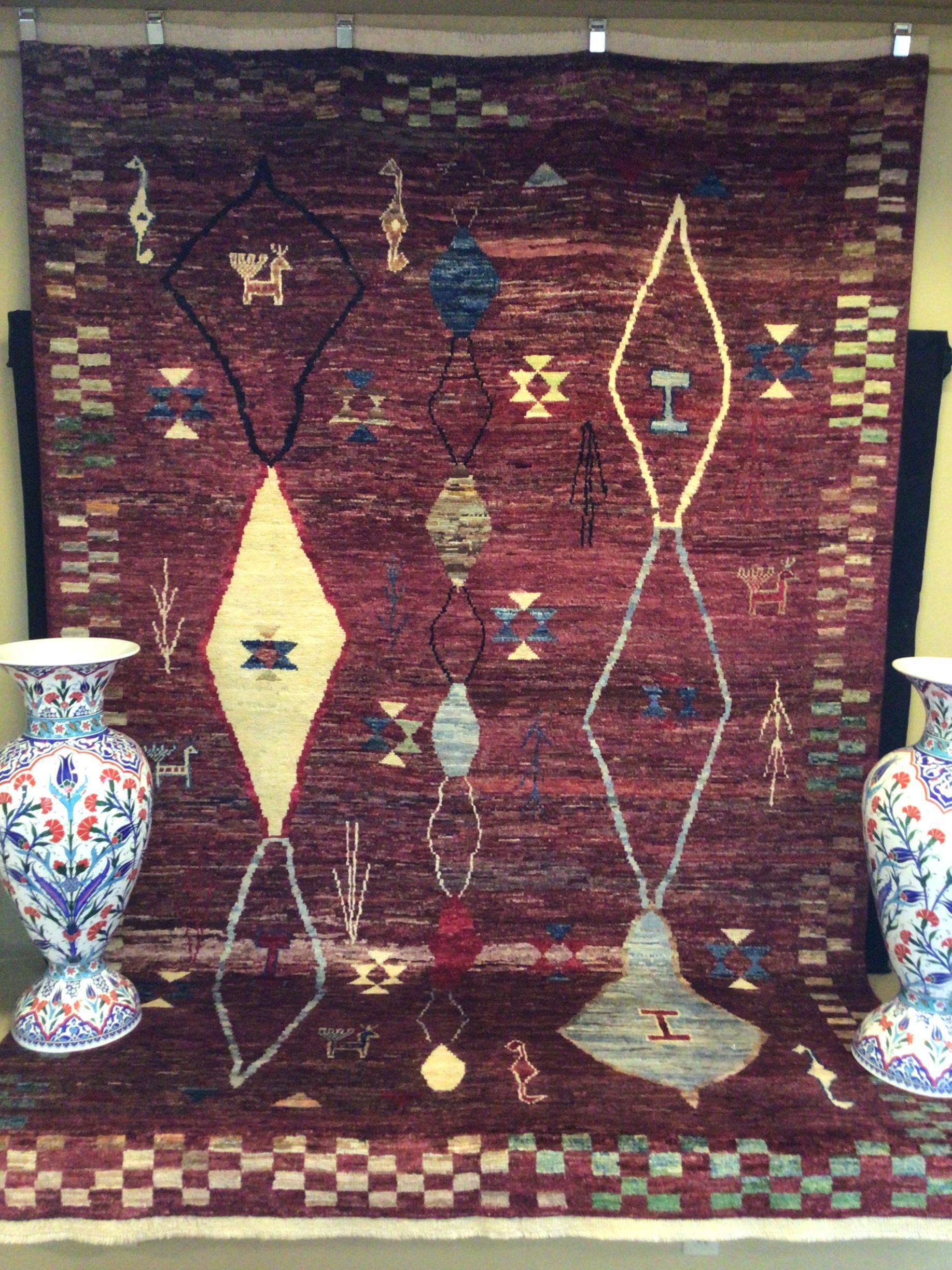 A rug is hanging on a wall next to two vases.