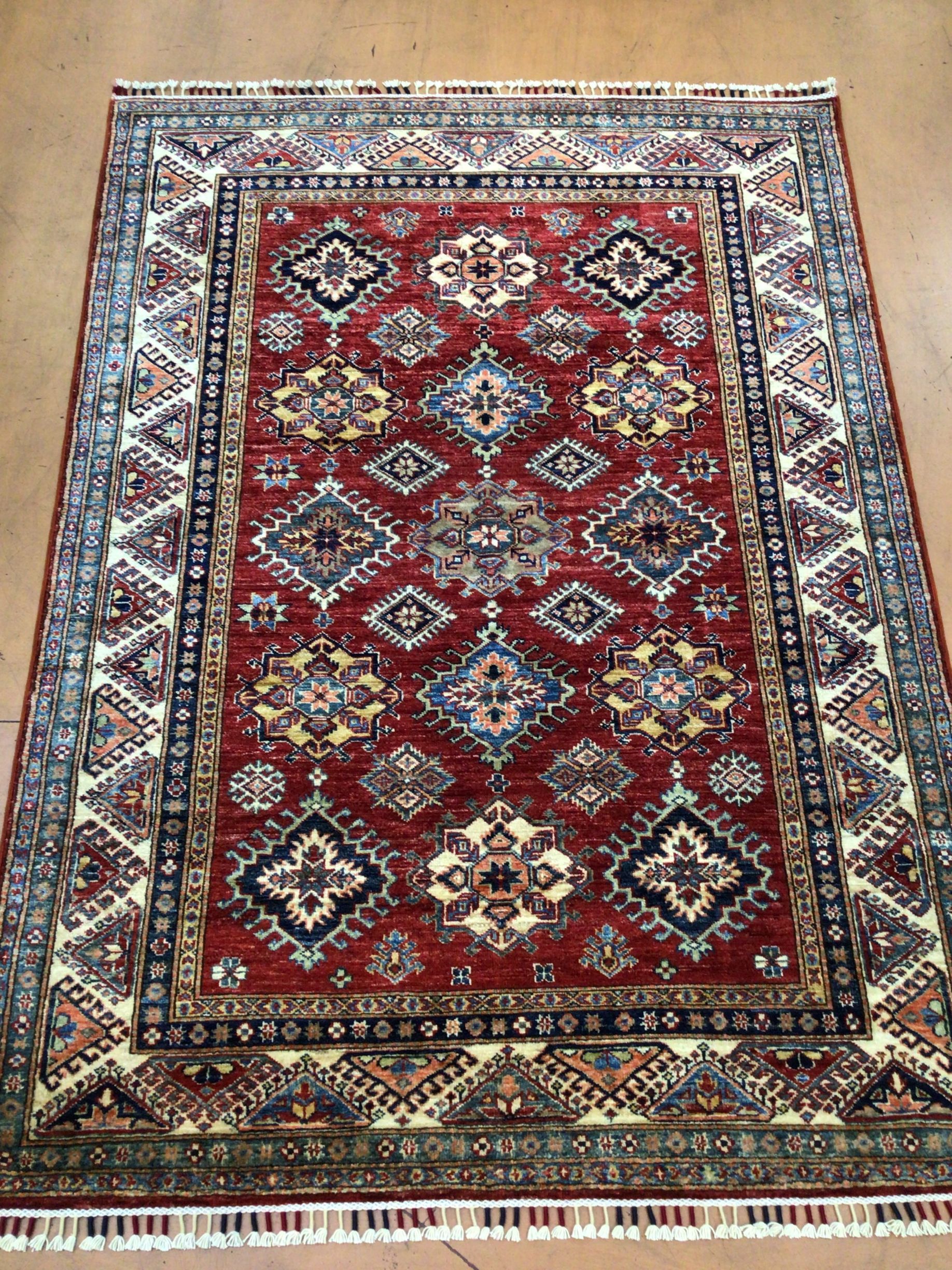A red rug with a blue border is sitting on a wooden floor.