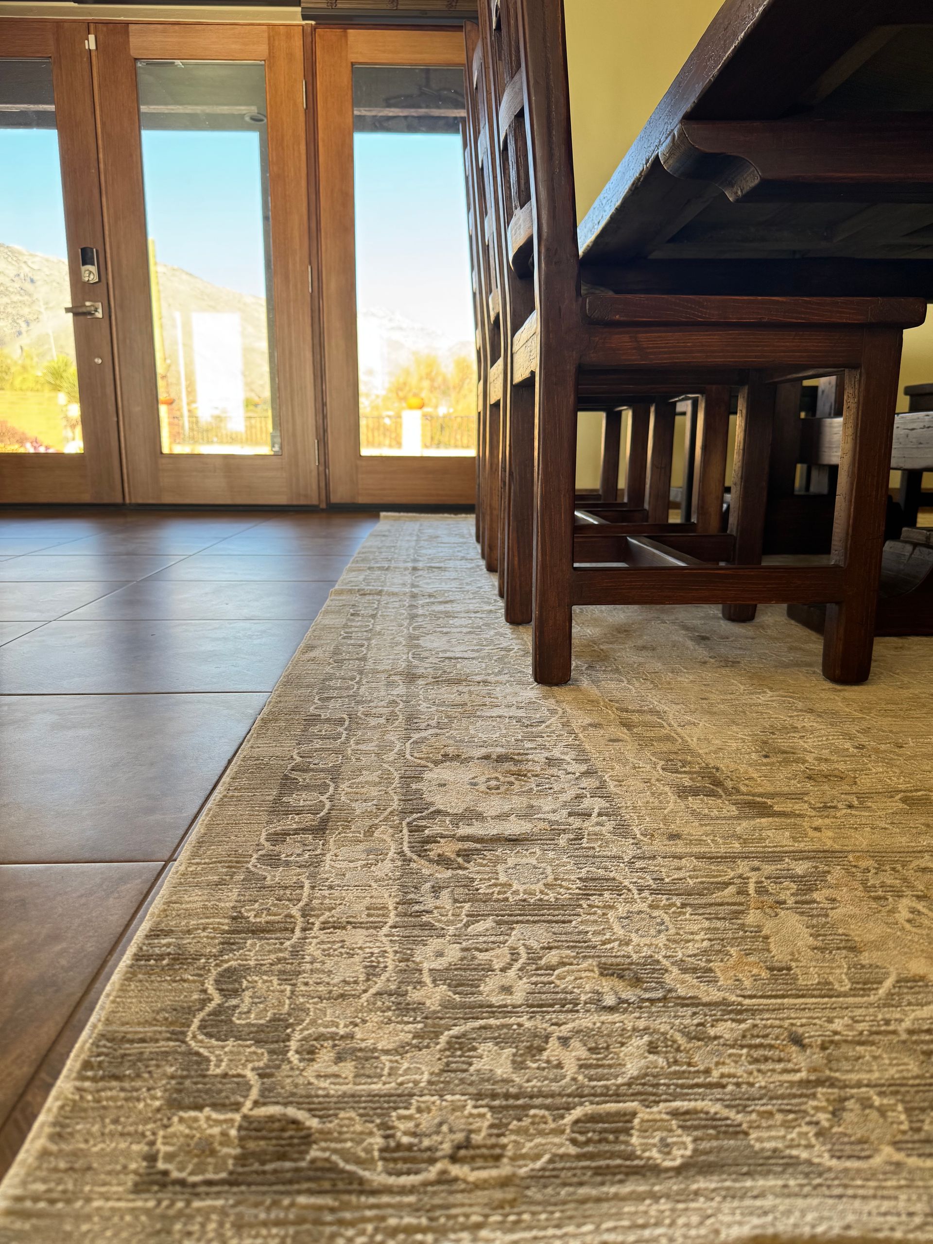 A dining room with a table and chairs and a rug on the floor.