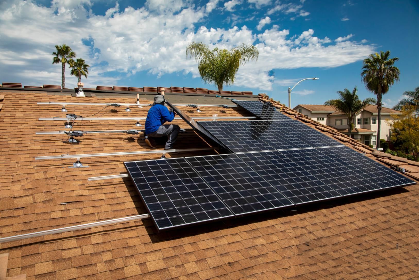 A man is installing solar panels on the roof of a house.