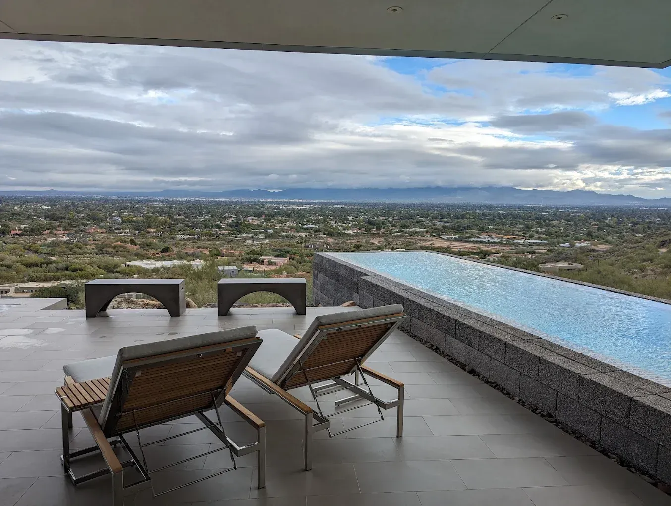 Two lounge chairs are sitting on a patio next to an infinity pool.