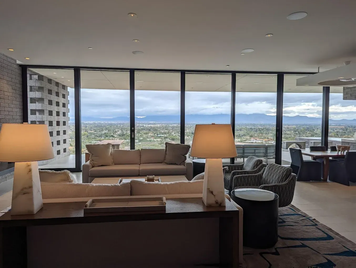 A living room with a couch , chairs , lamps and a large window.