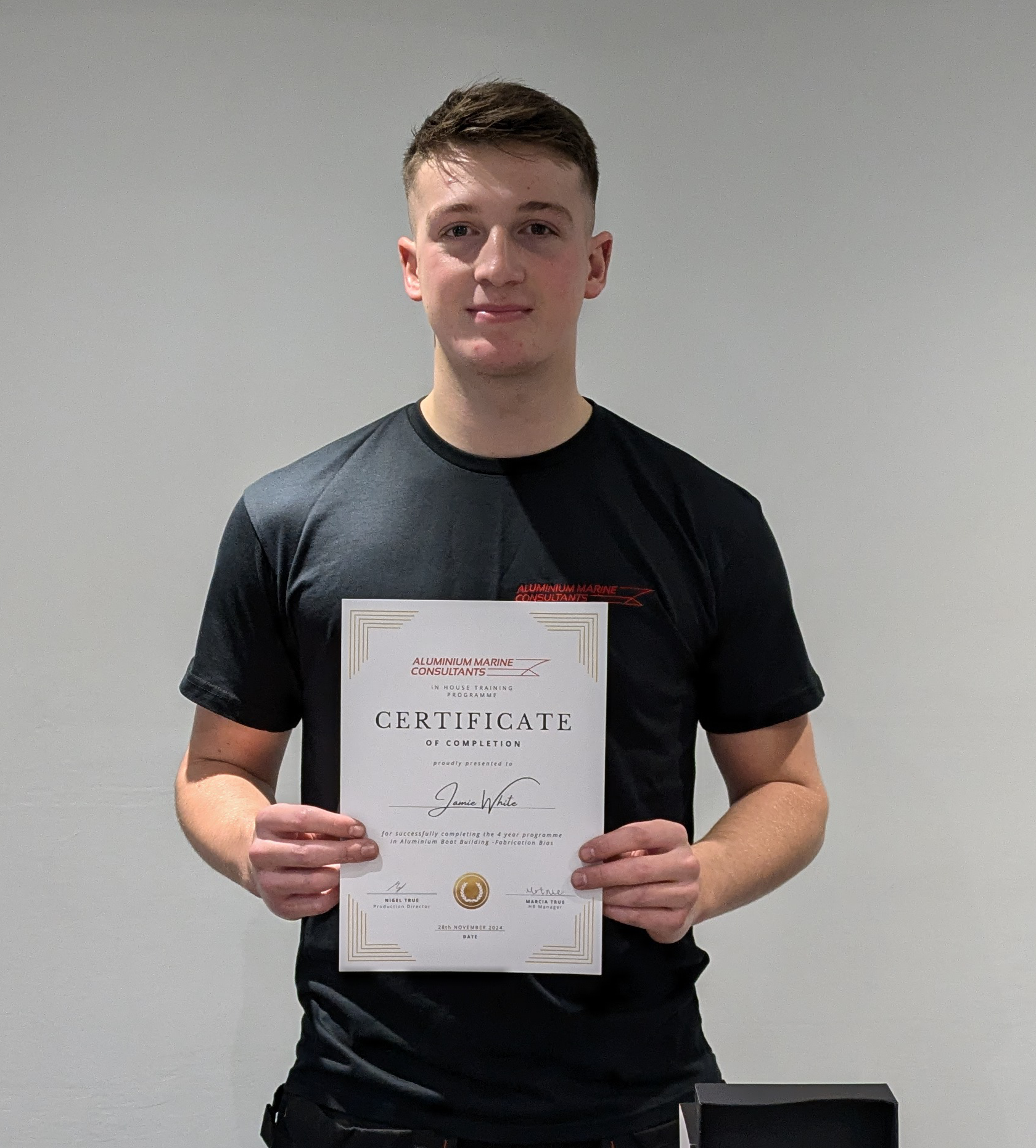 A young man in a black shirt is holding a certificate