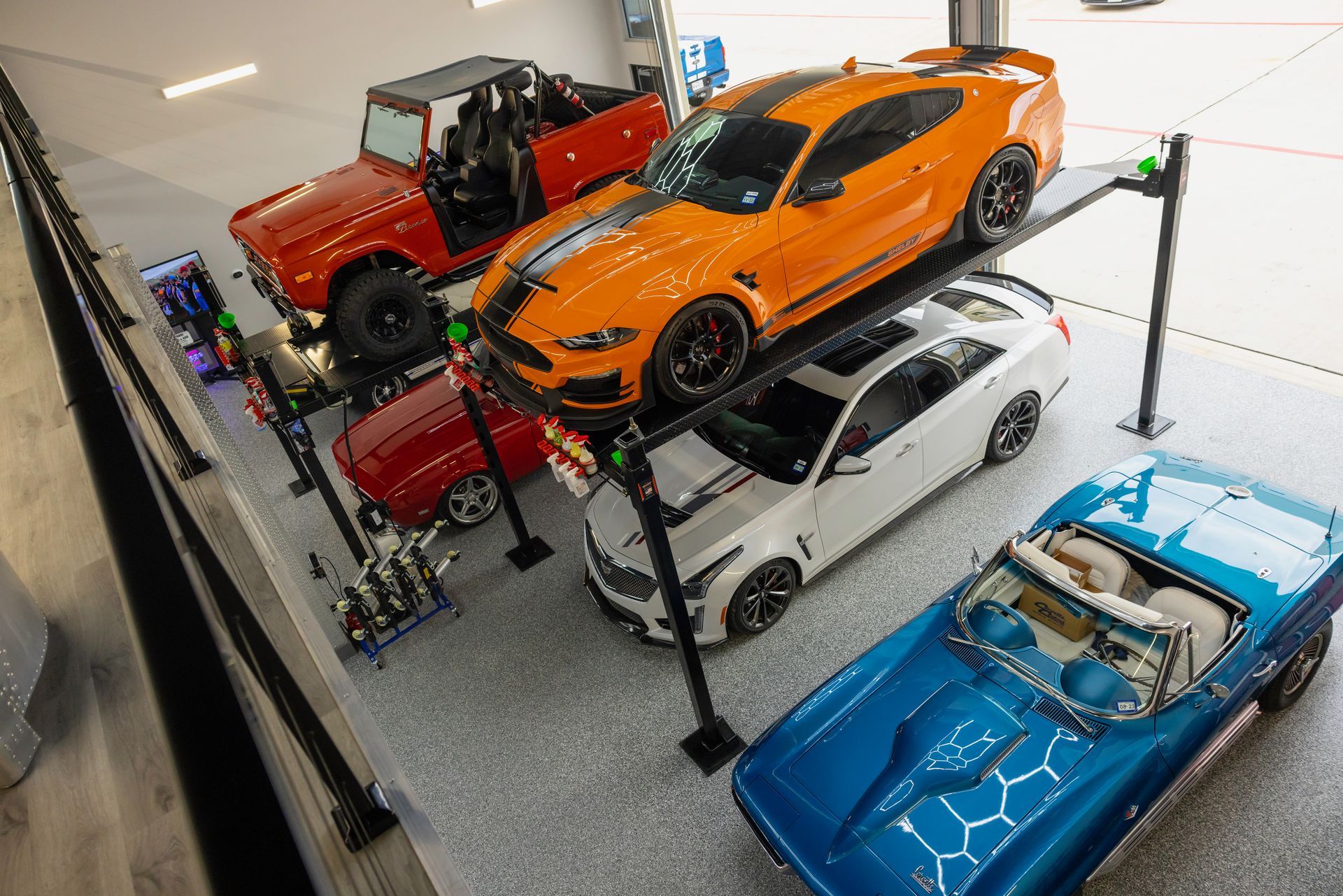 Collection of cars in a garage, including a red Bronco, orange Mustang on lift, and blue convertible. | Auto Motive