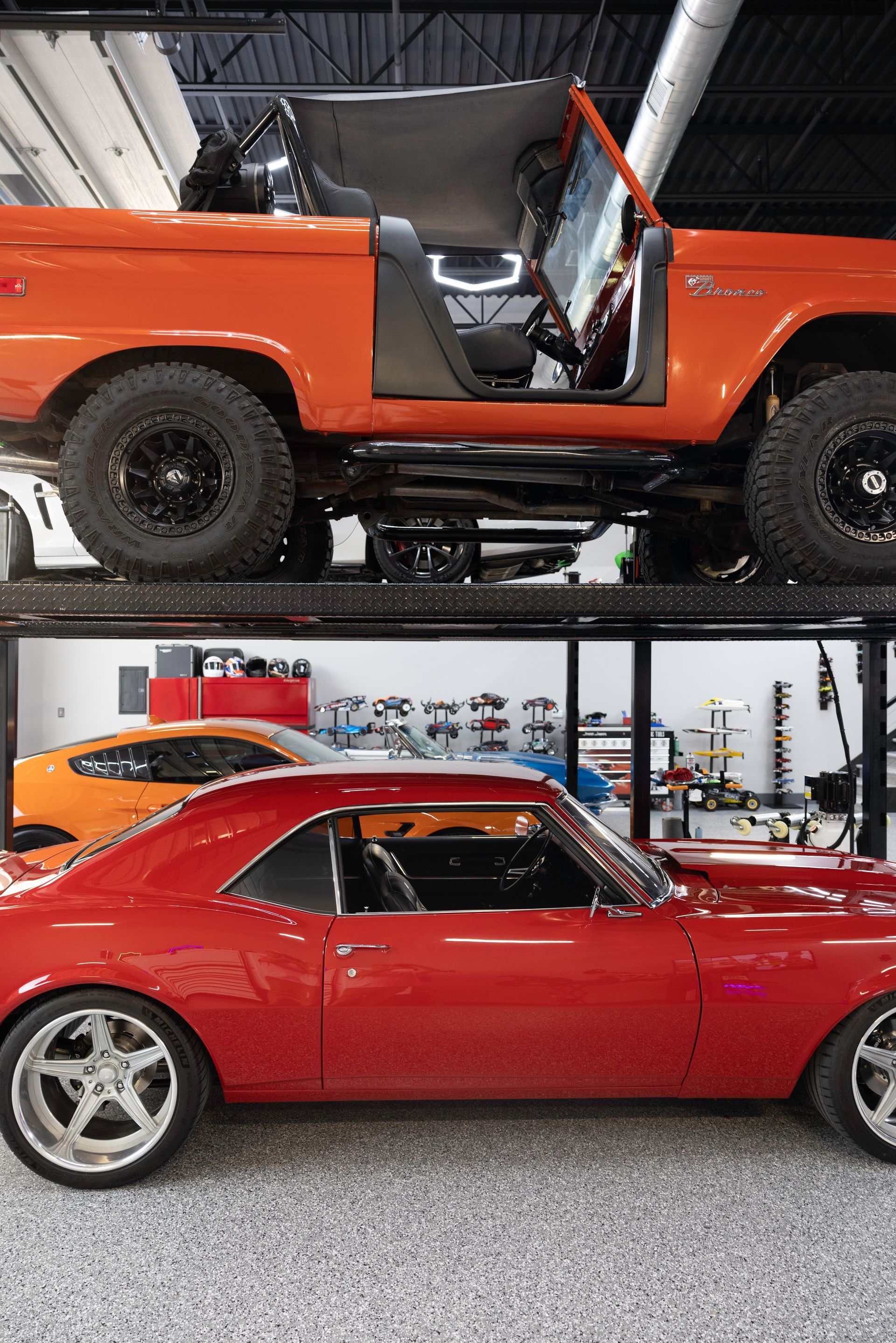 Red vintage car parked under a lifted orange Bronco in a garage. | Auto Motive