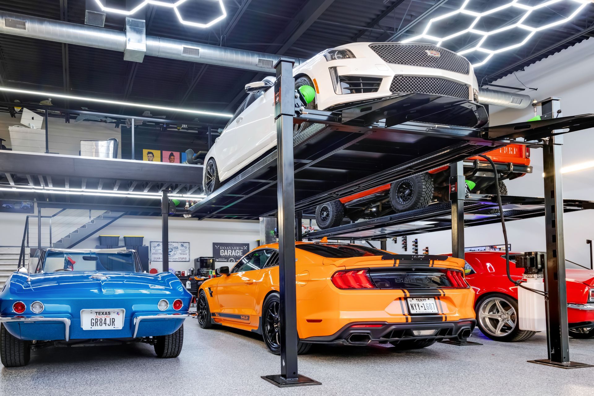 Garage filled with classic and modern cars, including a blue Corvette and orange Mustang, with car lifts. | Auto Motive