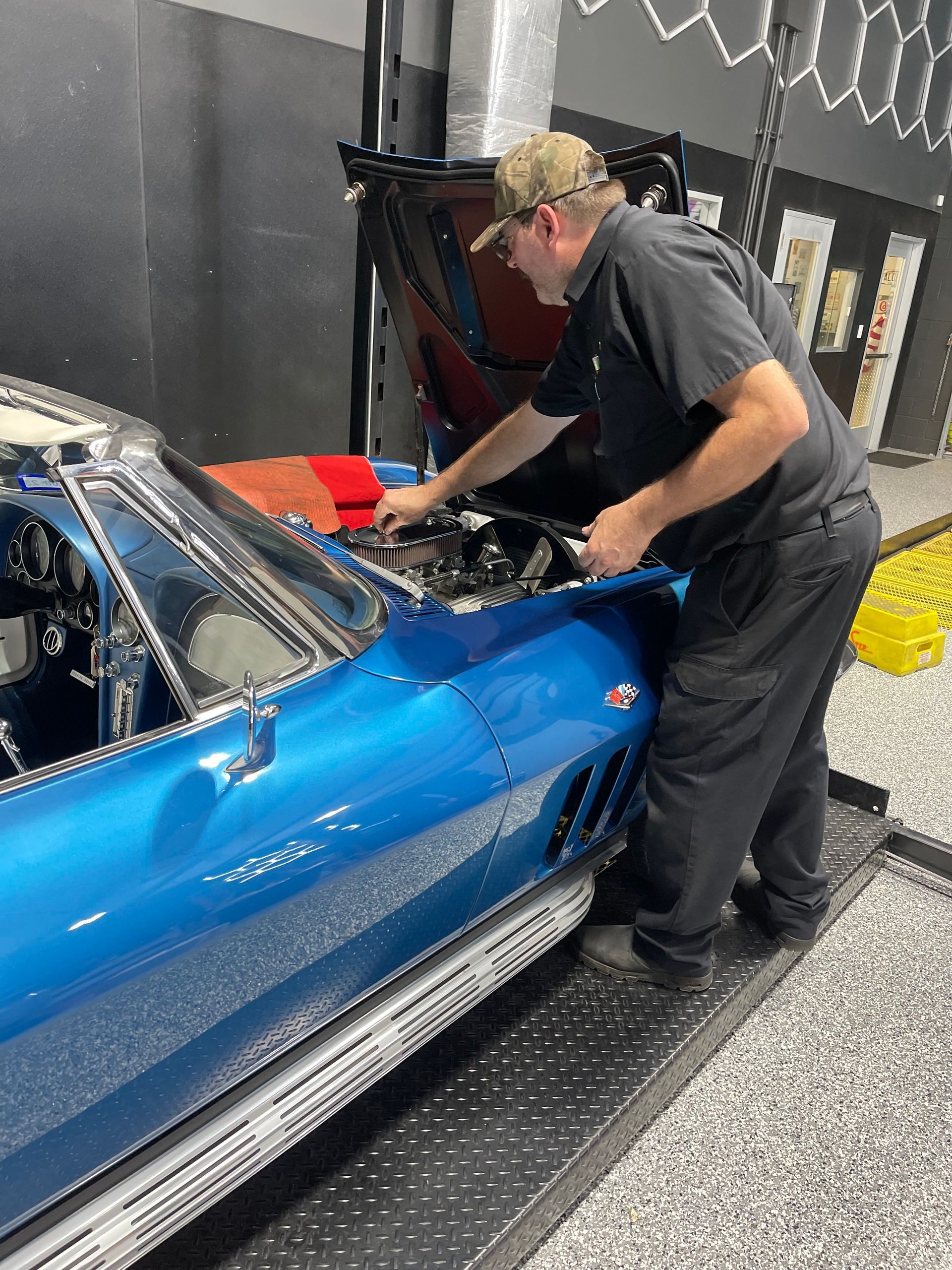 Mechanic in a garage working on a bright blue classic Corvette.