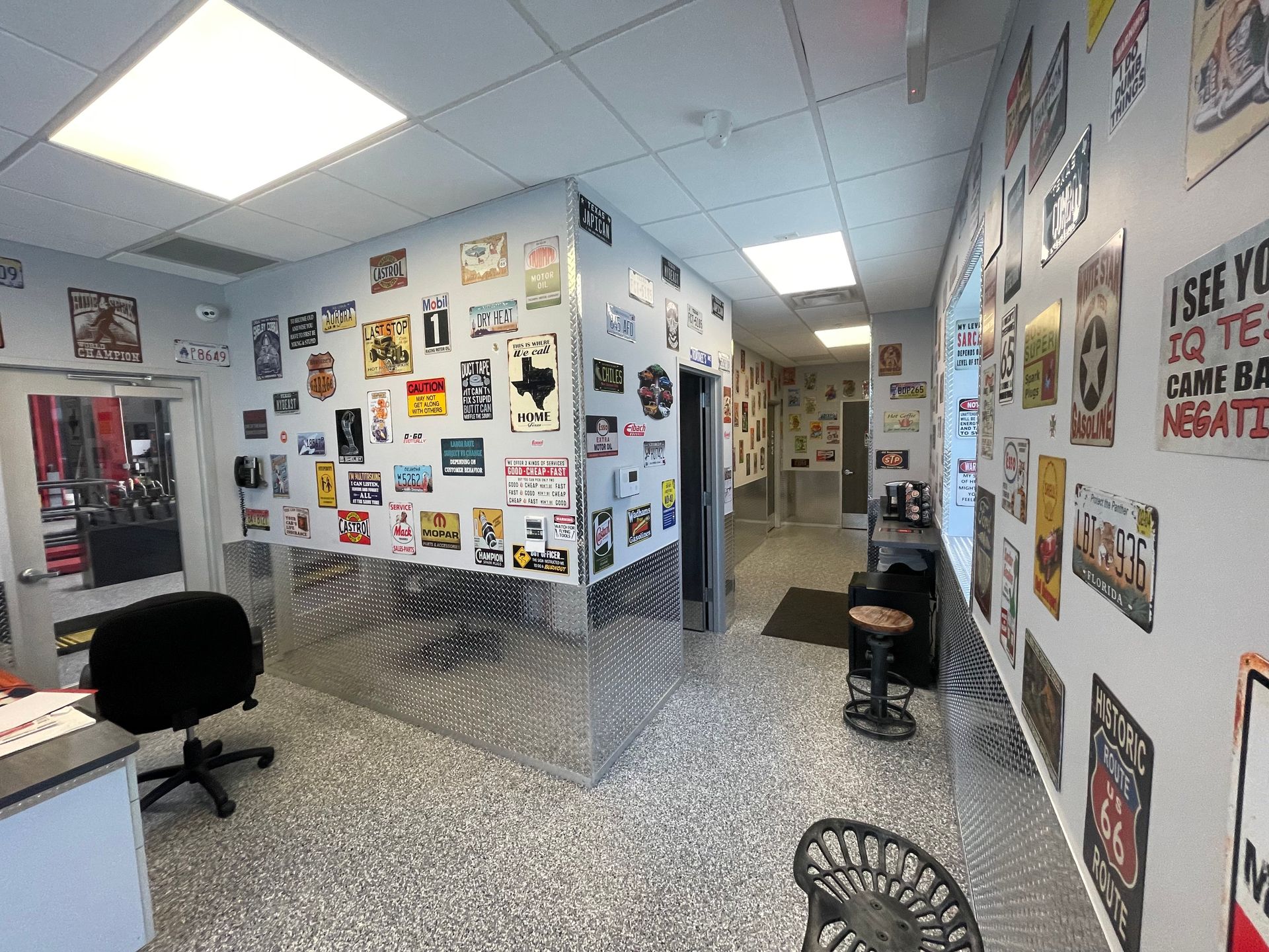 Interior view of a shop with many metal signs on walls. Office desk and chair in the foreground. | Auto Motive