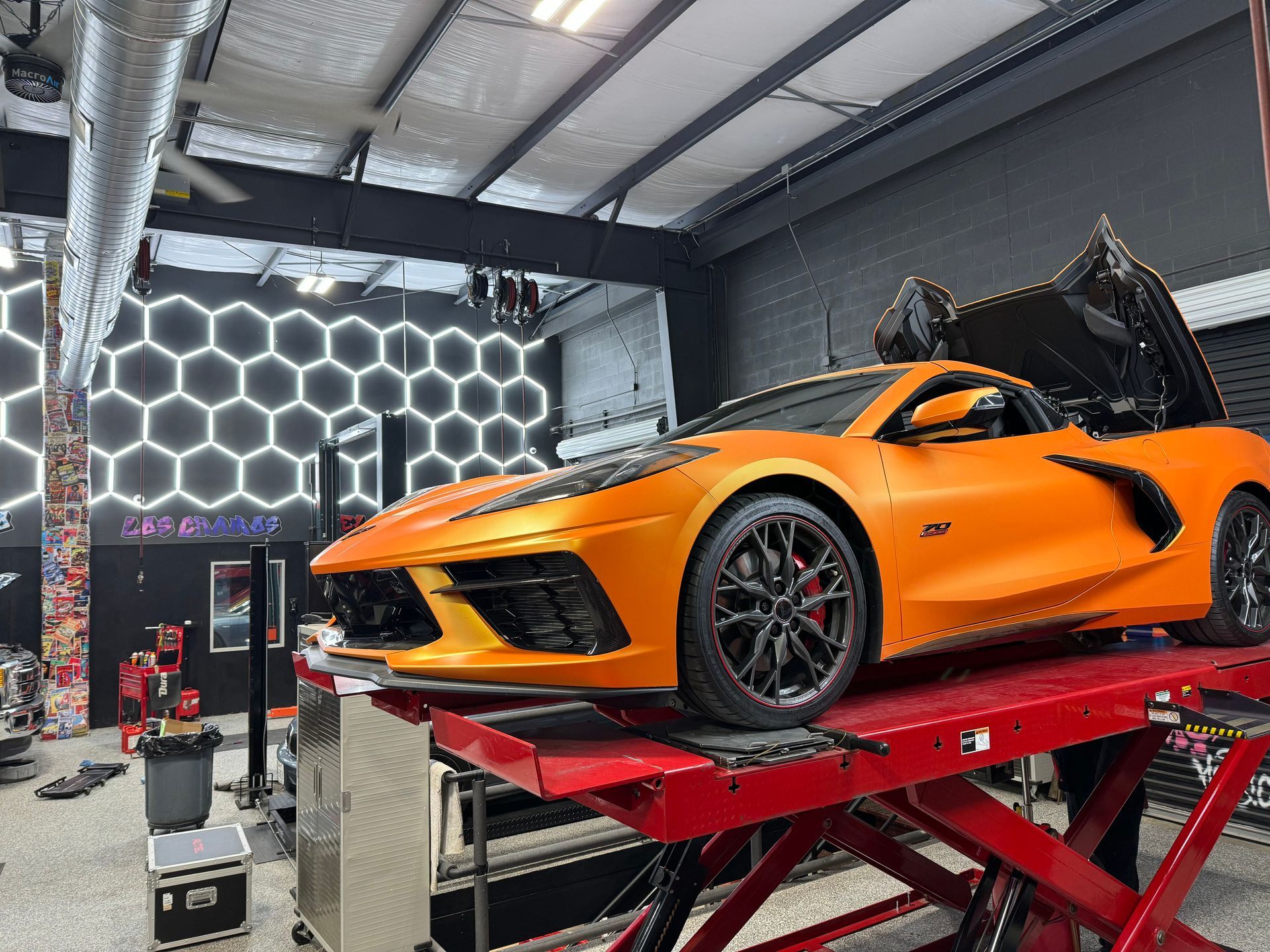 Orange sports car on a red lift inside a garage with honeycomb lights. | Auto Motive