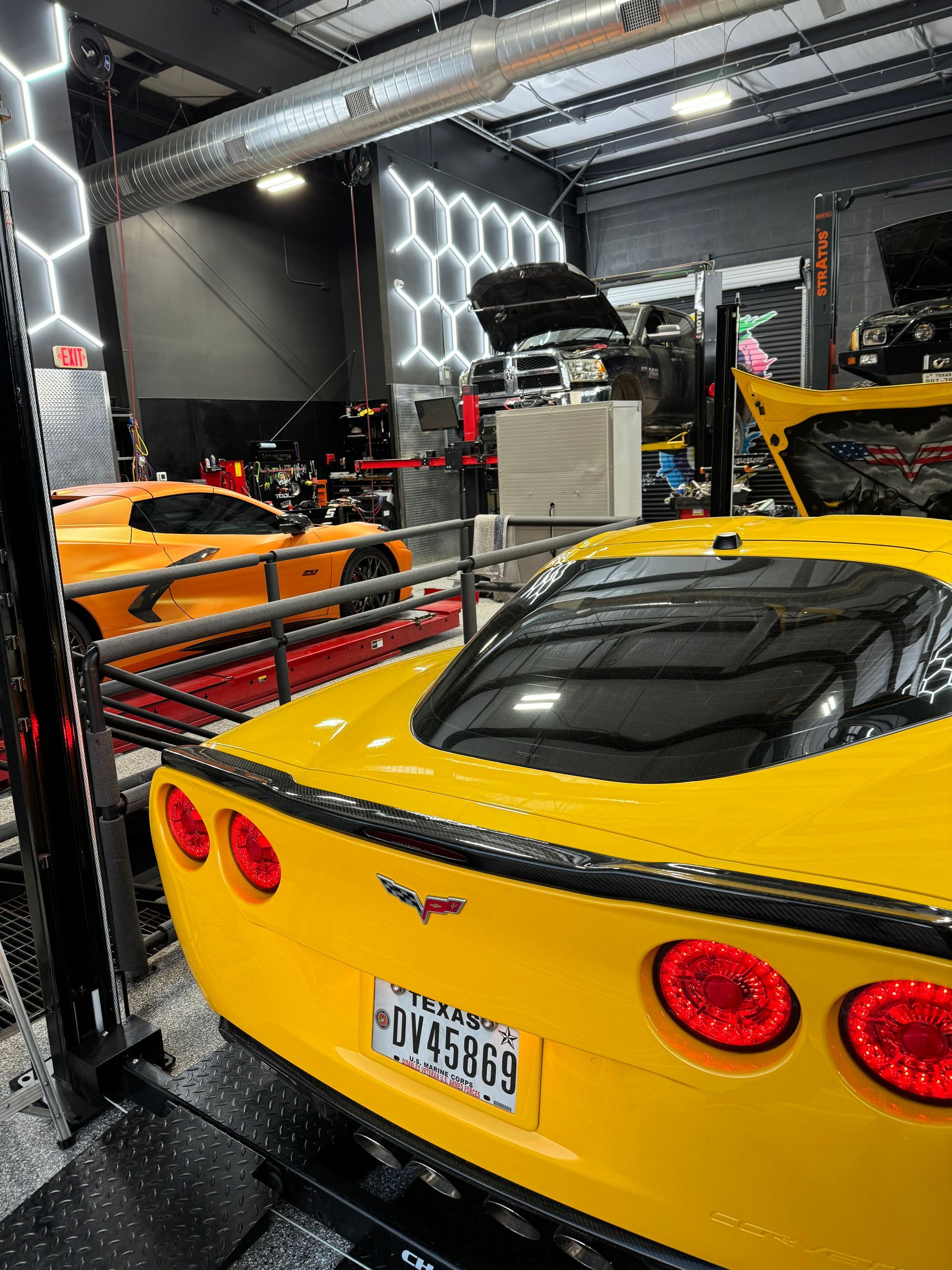 Yellow Corvette in a garage with other cars. | Auto Motive