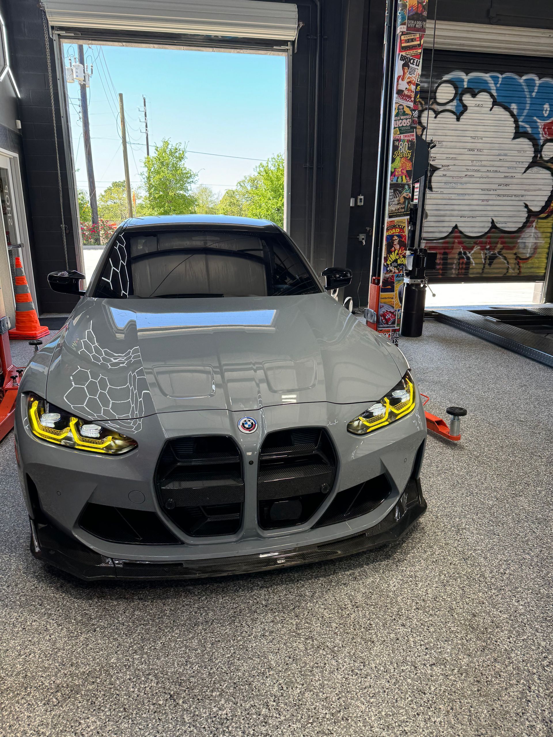 Gray BMW M4 with yellow headlights in a garage, a black front spoiler. | Auto Motive