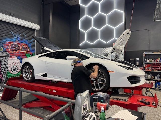 Mechanic working on white Lamborghini in a garage. The car is on a lift.
